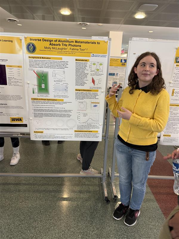 A researcher stands beside a large academic research poster mounted on a display board in an indoor campus atrium.